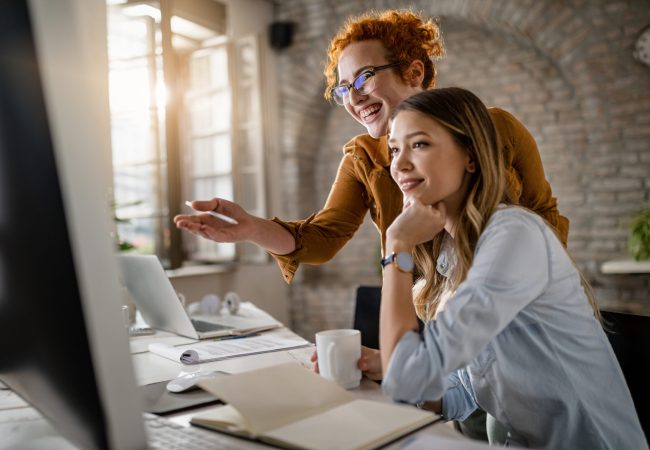 Happy female entrepreneurs reading an e-mail on computer while working together in the office. Focus is on redhead woman.